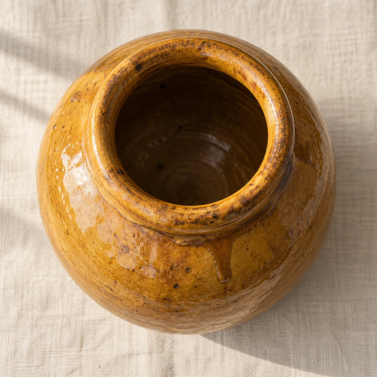 An ochre glazed vessel with an uneven glaze and a thick rim.