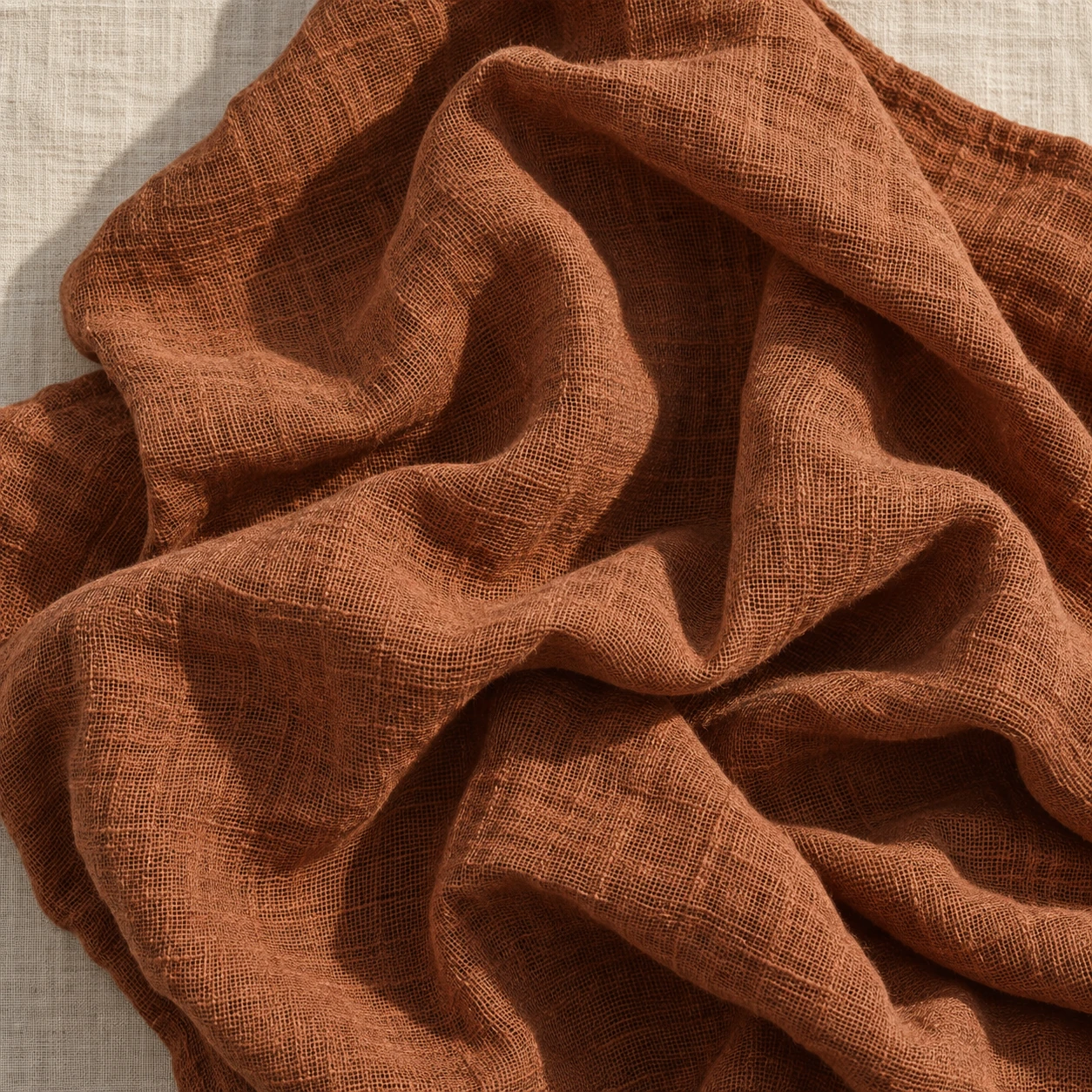 Crumpled rust linen, open weave, the creases holding shadow.