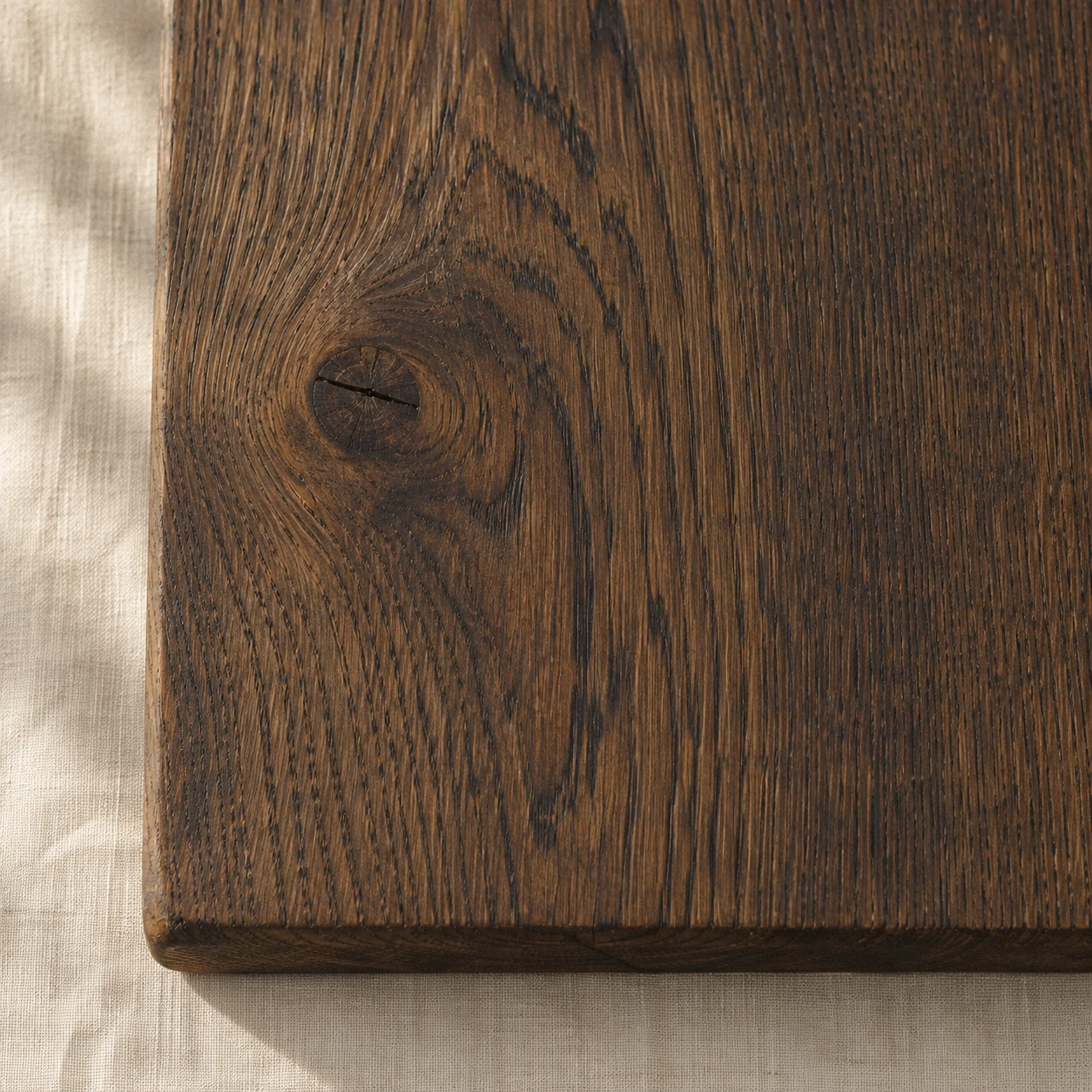 The edge of a dark oak board with strong grain and one knot.