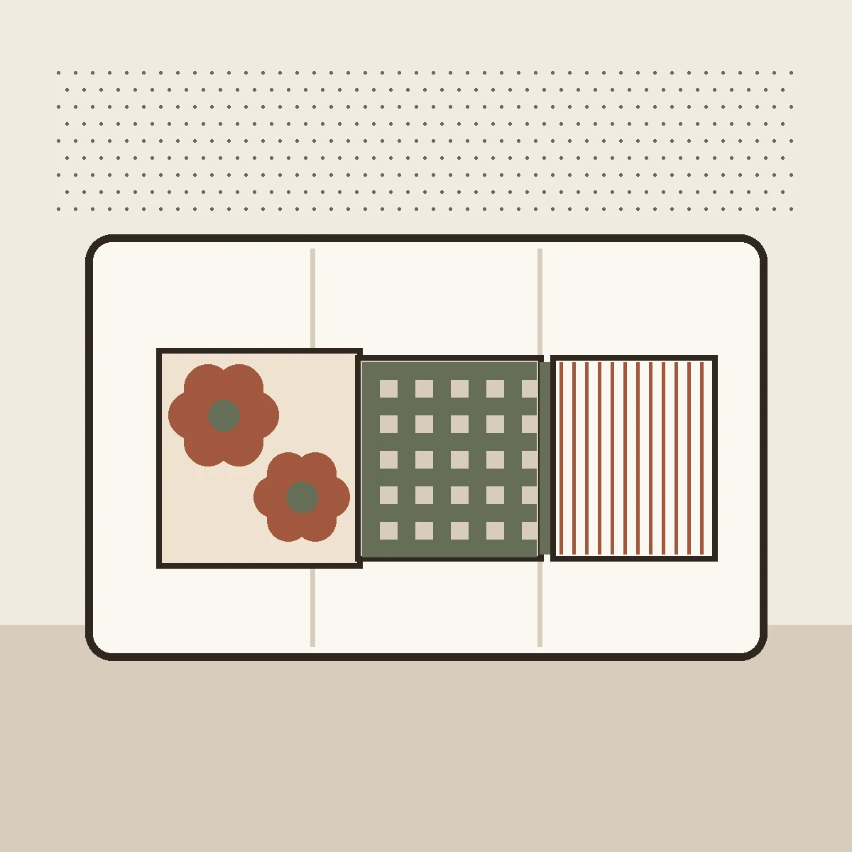 A two ink print of a cream sofa seen straight on with three cushions, each printed at an obviously different size: one bold flower that fills its cover, one middling check, one narrow stripe.