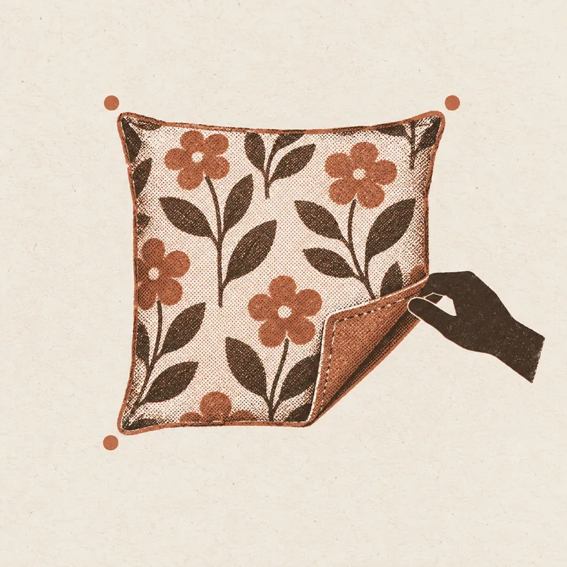 A hand folding back the corner of a floral pillow cover to show the plain fabric underneath, with a dot marking each corner of the pillow.