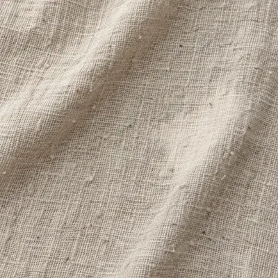 The same oatmeal linen after four years: the weave relaxed and pilled, two soft creases across it, one patch a shade paler.