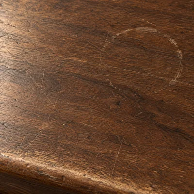 The same walnut after four years: fine scratches, one pale ring from a glass, and an edge rubbed lighter.